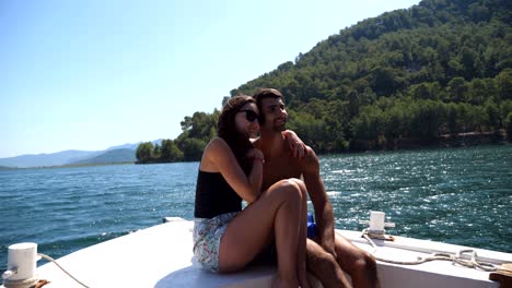 young pair sitting on bow of boat and posing to photographer at sunny day. happy couple in love spending time together on deck of ship and enjoying summer travel. concept of vacation or holiday. close up