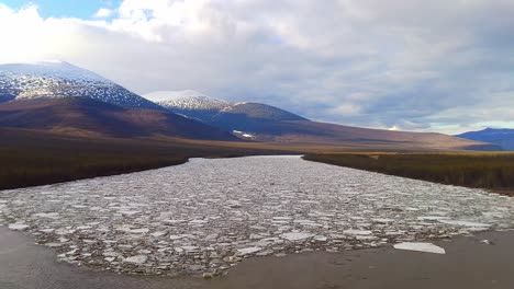 las montañas cubiertas de nieve y el río parcialmente congelado crean una escena serena en rusia cuando el hielo comienza a derretirse bajo un cielo nublado a principios de primavera.