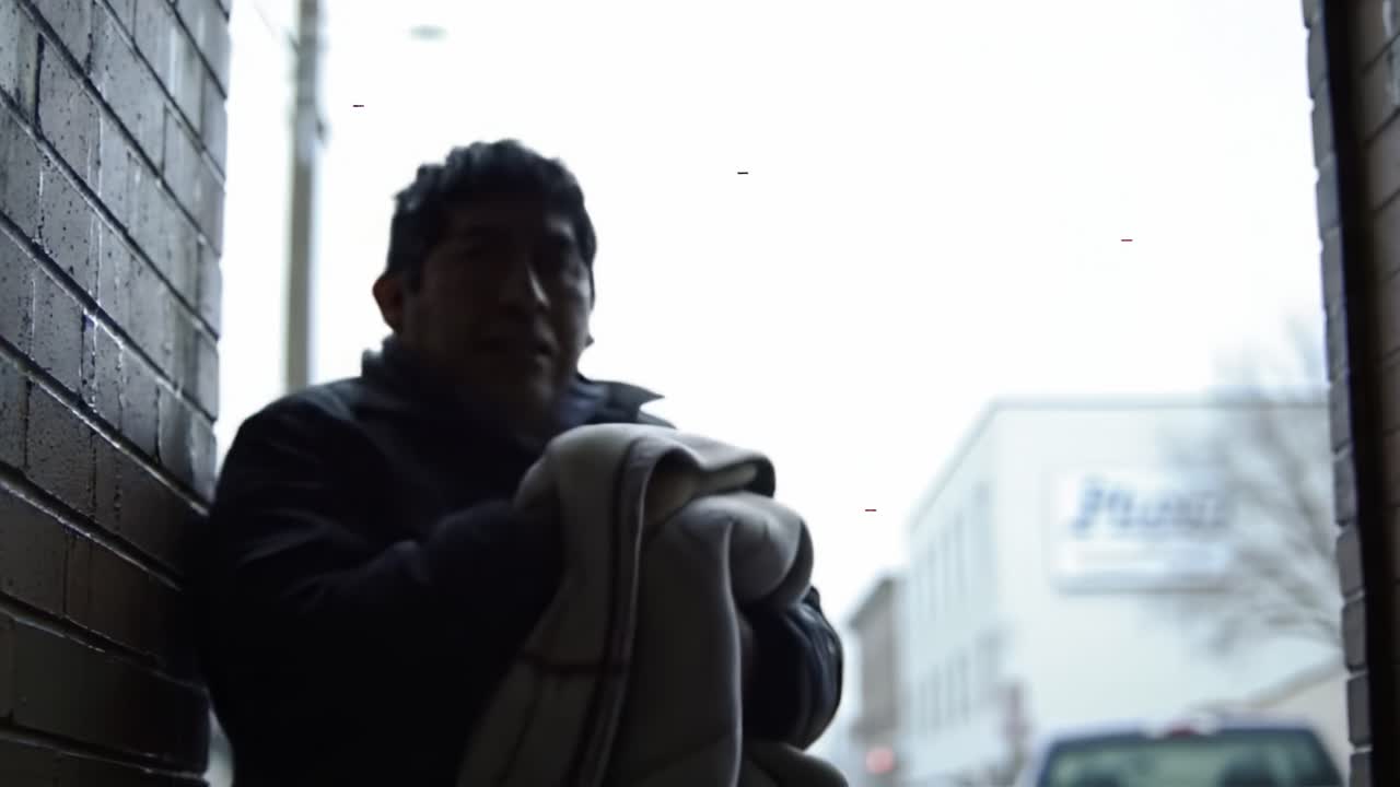 A Quiet Moment of Reflection: A Person Seated in an Alleyway, Wrapped in a Blanket, Observing the World Beyond the Brick Walls on a Gloomy Day