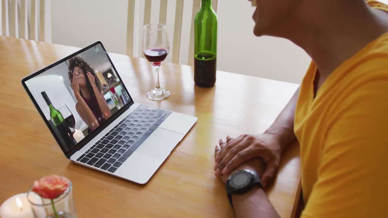 Mixed race man sitting at table using laptop making video call with female friend