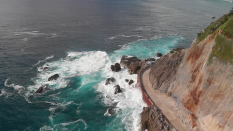 aerial drone tilt up next to ocean road with cliffs, crashing waves next to beautiful summer island