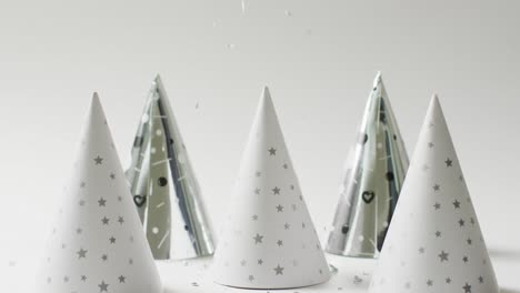 Video-of-four-white-and-silver-party-hats-on-pale-grey-background