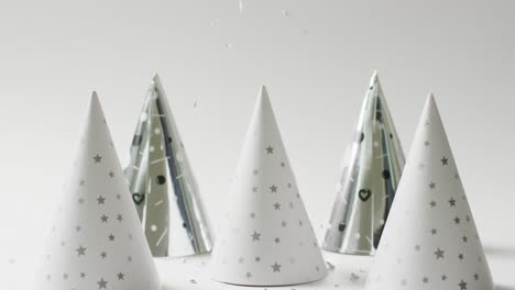 video of four white and silver party hats on pale grey background