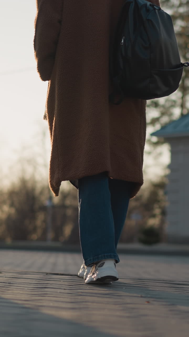 A girl is walking through a blurred park setting, with the shot starting from her legs and feet. . The background is softly out of focus