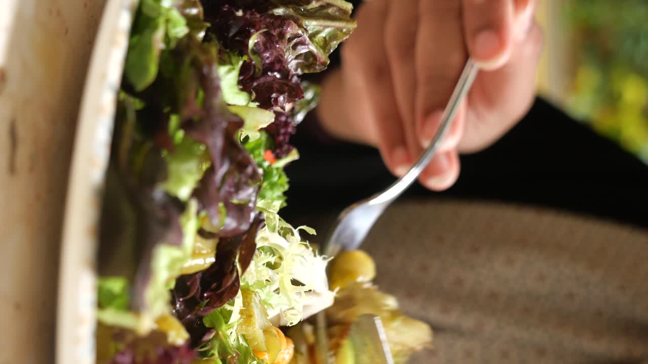 A close-up of a vibrant salad with fresh greens and other ingredients, being eaten with a fork