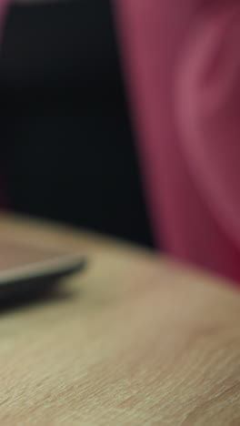 primer plano de una computadora portátil en una mesa de madera con una persona sosteniendo una hamburguesa en una mano y una taza de café en la otra, colocando suavemente el café de nuevo en la mesa, el fondo está borroso