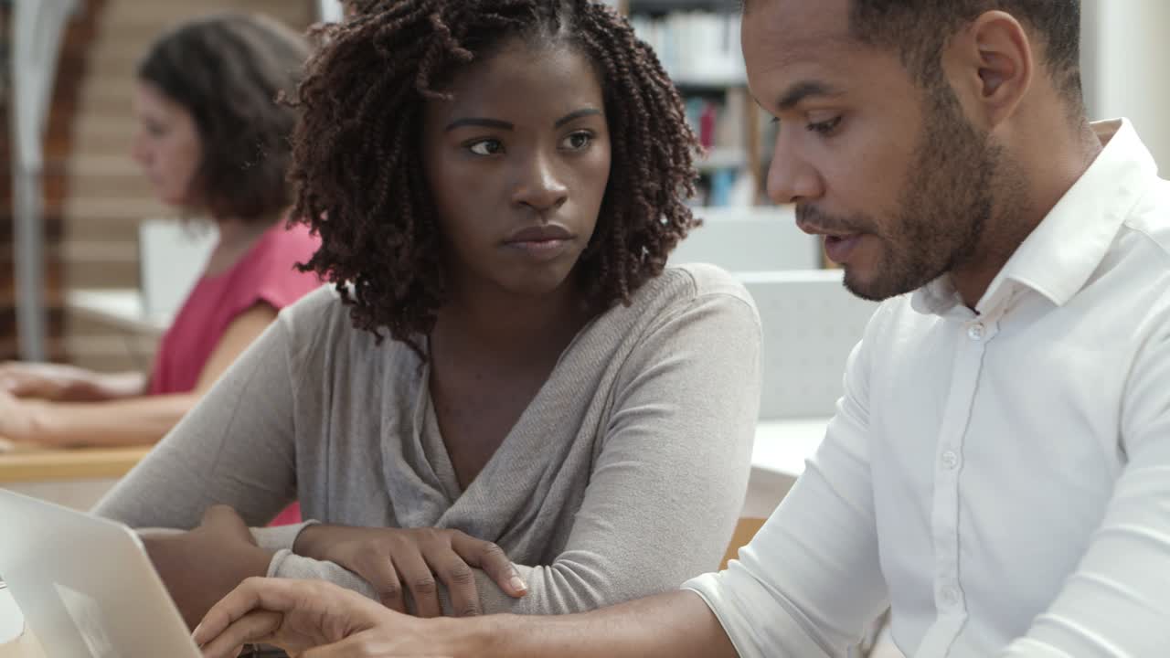 dos personas pensativas que trabajan con una laptop en la biblioteca pública