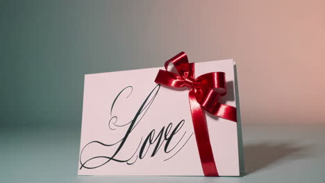 a white greeting card with the word 'love' in cursive and a red bow