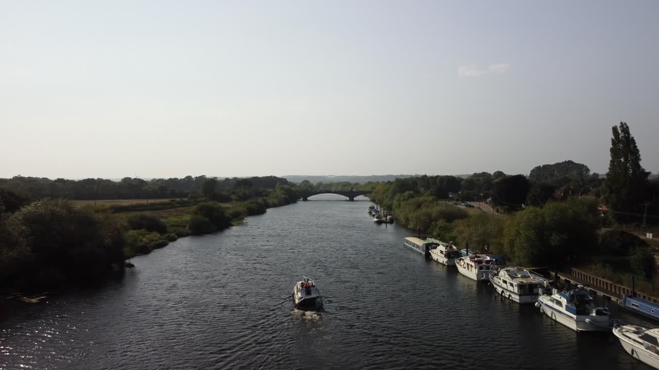 A River Boat forward along the river past many parked, moored boats on a long stretch of the River Trent in the Nottinghamshire countryside.
