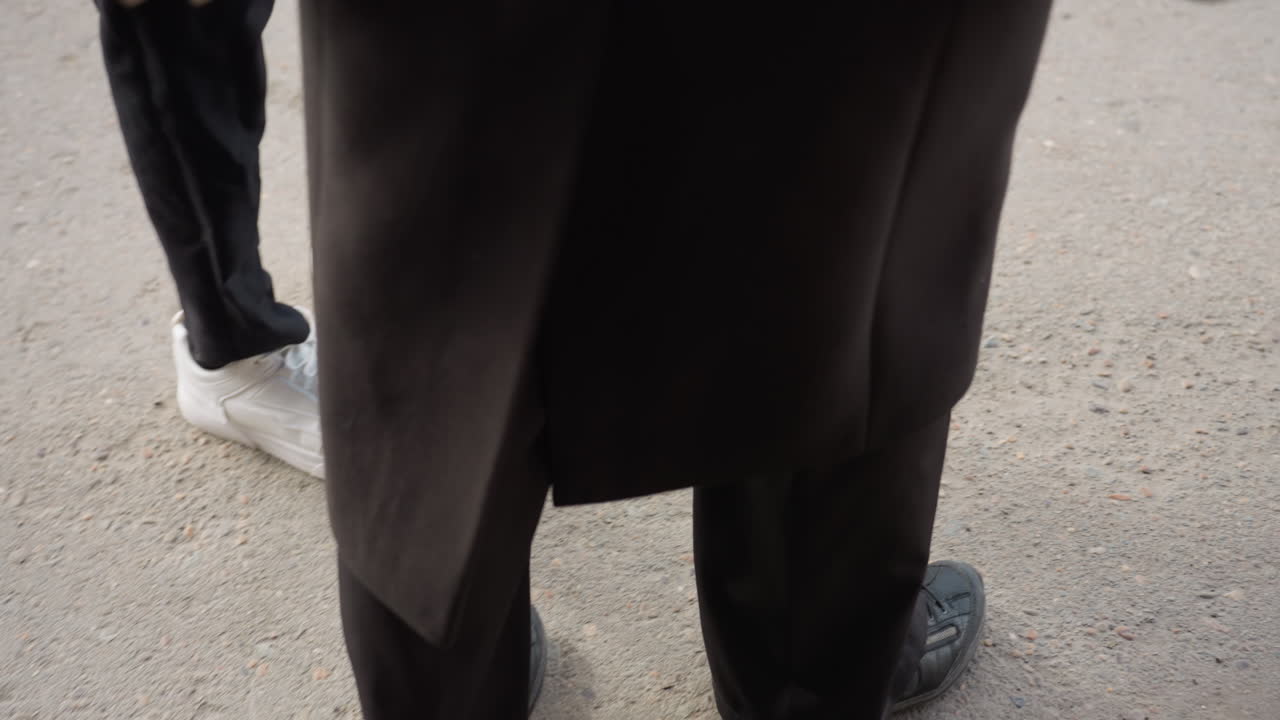 Vista dall'alto di una persona che scende le scale con scarpe scure, avvicinandosi all'entrata dove una seconda persona con scarpe da ginnastica bianche aspetta mostrando gradini consumati, corrimano in metallo, movimento e momento di routine quotidiana