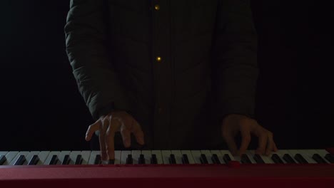 close up front view of an elegantly dressed man playing the piano with both hands in a darkened room