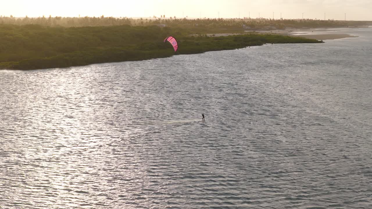 Kitesurfer rides on shallow lagoon near Ilha do Guajiru Itarema Ceará Brazil with steady trade winds and rippled water surface under warm sunset light, drone forward tracking shot