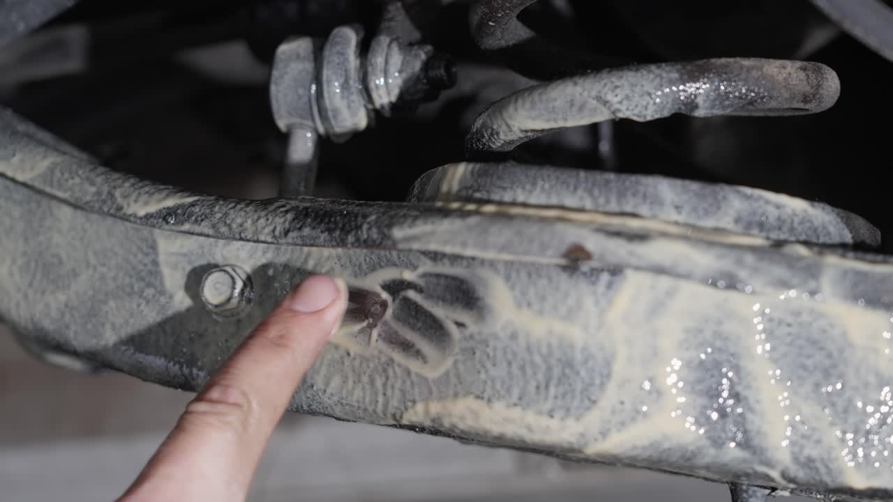 Man uses finger to show lanolin rust protection product freshly applied to car underside, close up