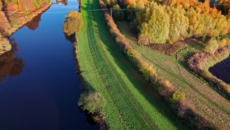 Imágenes-Aéreas-De-Drones-Del-Río-Que-Aún-Fluye-Con-Un-Espejo-Como-Reflejo-Del-Cielo,-Con-Camino-De-Hierba,-Pasarela-Y-árboles