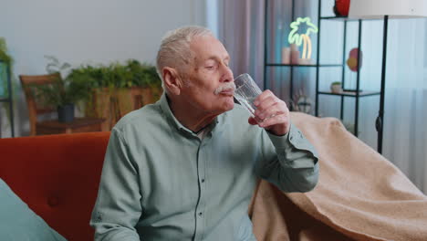 Un-Abuelo-Sediento-Sentado-En-Casa-Sosteniendo-Un-Vaso-De-Agua-Natural-Haciendo-Sorbos-Bebiendo-Agua-Sin-Gas