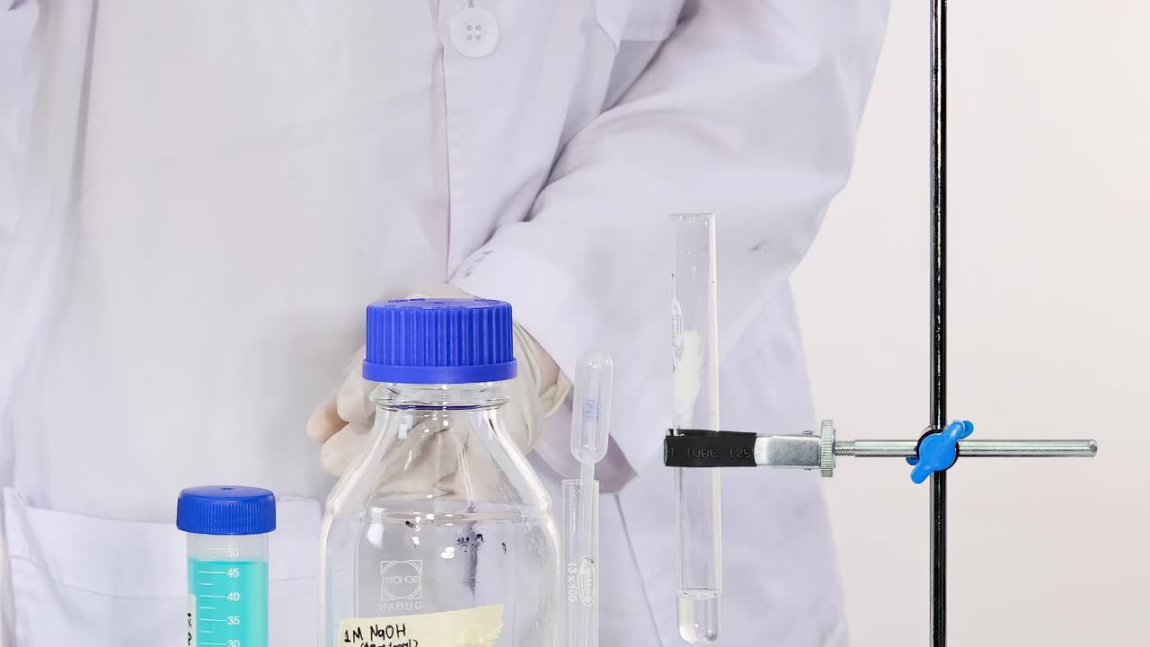 A scientist in a lab coat handles a NaOH bottle and test tube with precision and care.
