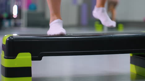 close-up lower angle view of individual stepping onto exercise bench and stepping down during workout, gym environment with fitness equipment in background