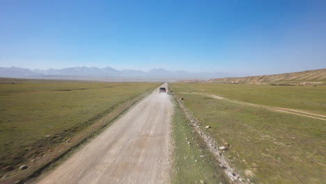 Tracking-drone-shot-of-a-vehicle-on-a-dirt-road-driving-near-Kel-Suu-lake-in-Kyrgyzstan,-drone-closing-the-distance
