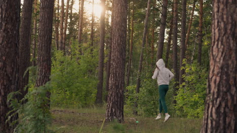 woman in hood runs in forest at sunset. sports routine with cardio exercise to improve physical health and relieve stress after work in evening