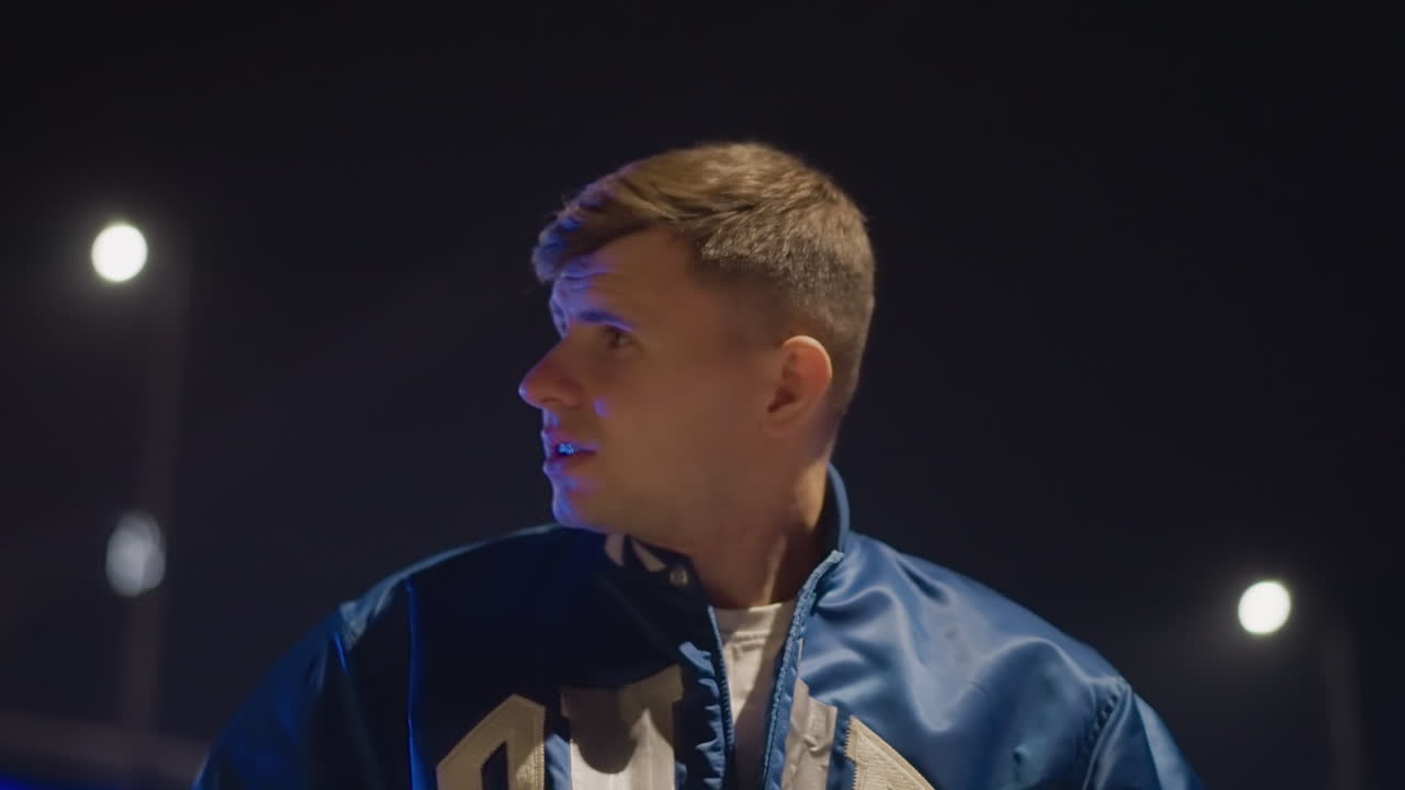 Man gazes over shoulder under streetlights, Contemplative male figure facing away in nighttime setting with car lights, Poignant image of man pondering in dark with distant illuminated vehicles