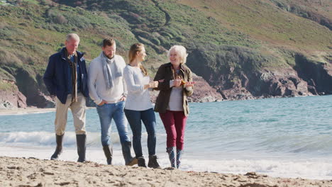 senior couple walking along shoreline with adult offspring on winter beach vacation