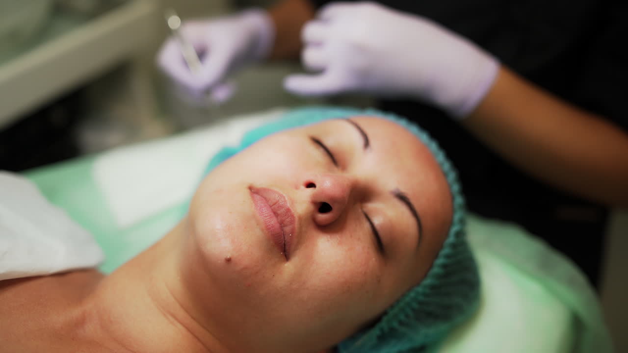Relaxed Caucasian woman in a cap undergoing face skin care procedures at salon. Beautician uses blackhead removing instrument. Close up.