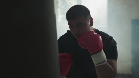 athlete does punches and block training in sports club. skilled sportsman beats punching bag in equipped gym against dust cloud slow motion. martial arts champion