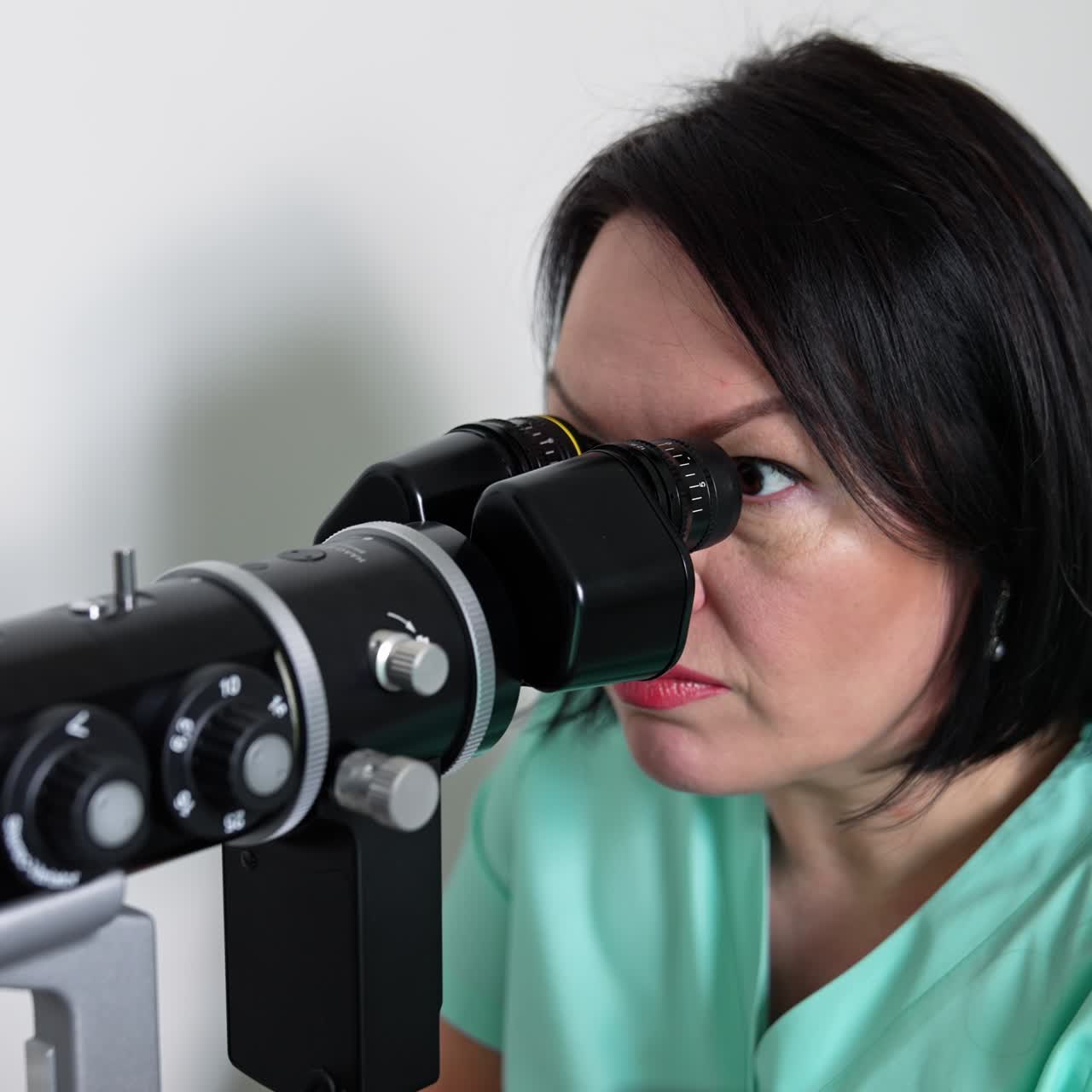 Adult female oculist doctor sits at the apparatus looking aside. Ophthalmic specialist uses advanced equipment to check patient's eyesight