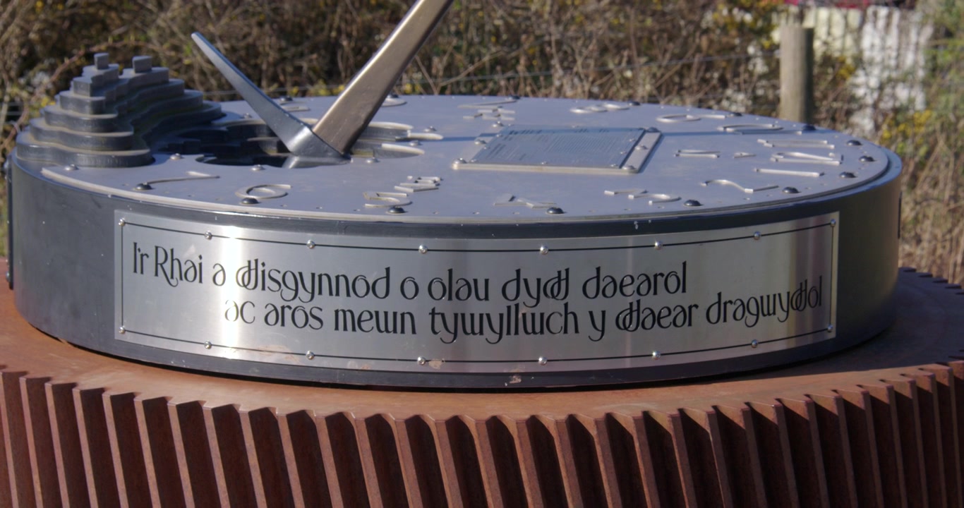Inquadratura a medio zoom indietro della meridiana commemorativa delle miniere di Bettisfield con un'iscrizione in lingua gallese