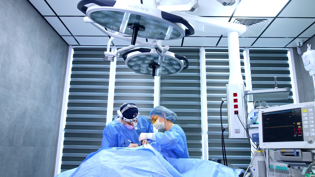Medics perform plastic surgery in modern well-equipped surgical room. Surgeon applies metal tool and electric device.