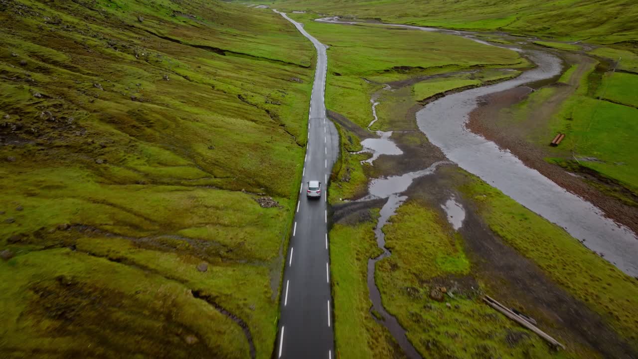 A car drives on a remote road between lush green hills in the Faroe Islands