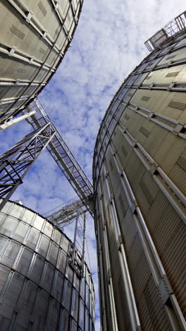 aluminum containers for storing grains. exterior of large metal elevators. close-up. view from below. camera motion around. vertical video