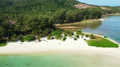 people sunbathe on white sand of exotic beach and swim on calm clear water of turquoise lagoon on tropical island with trees forest in thailand