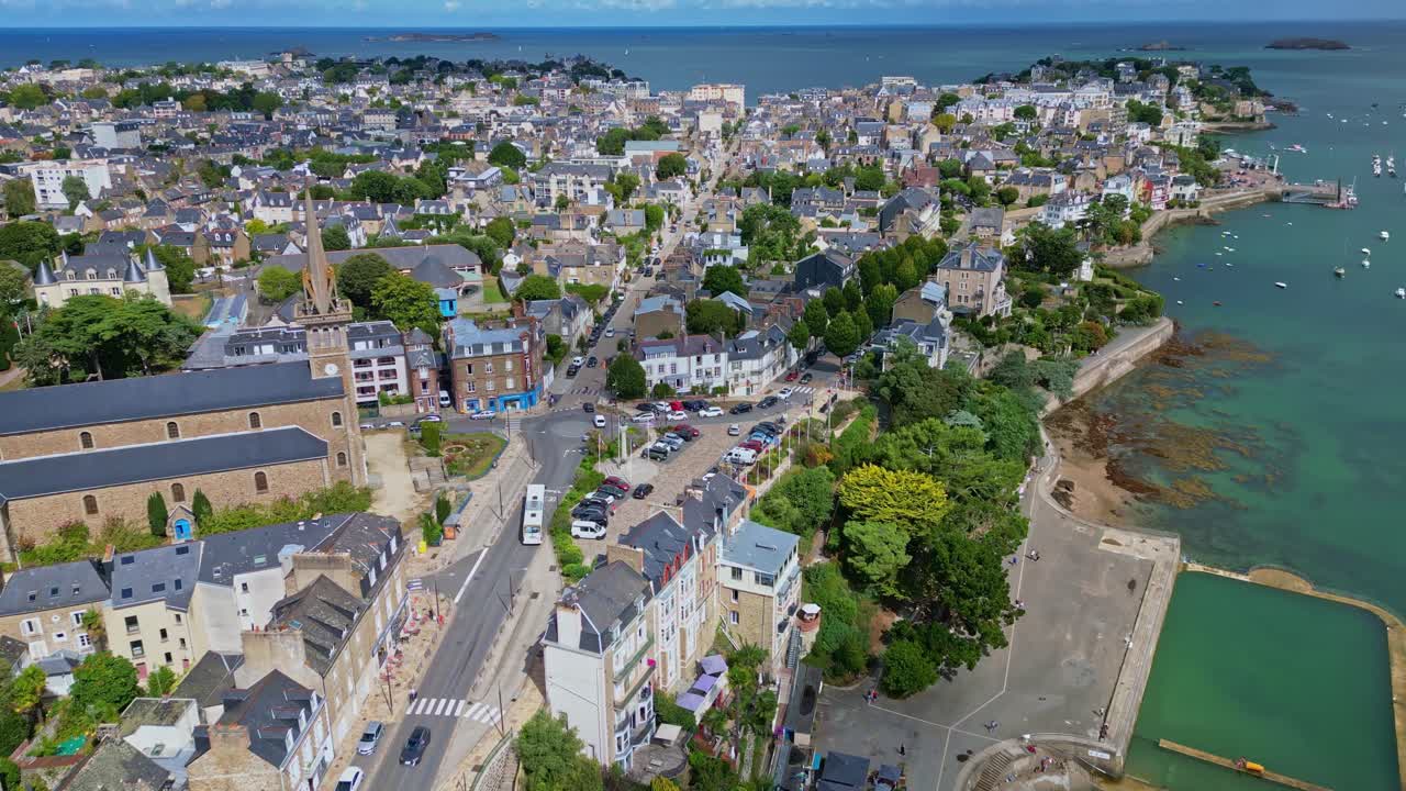 Panoramic aerial view showing the coastal town of Dinard in Brittany, France, with its historic buildings, urban landscape, beautiful coastline, and a rectangular sea pool, drone establishing shot