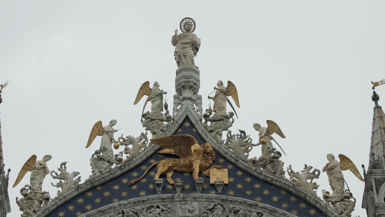 성 정문 상단에 있는 날개 달린 사자, 천사, 예수 그리스도의 조각상을 볼 수 있습니다.