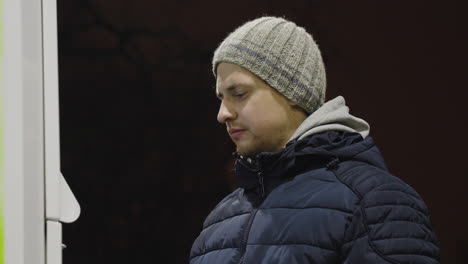 vista media mirando hacia arriba a un hombre blanco guapo en abrigo de invierno en la noche, mirando fijamente la pantalla de la gasolinera