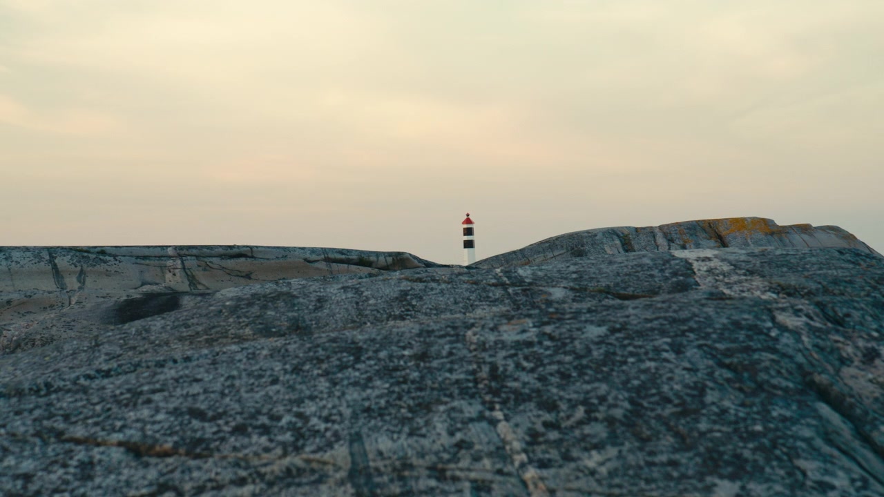 Paesaggio costiero minimalista con un faro distante che emerge sopra lisce scogliere di granito sotto un cielo serale dai colori tenui. Scena marittima calma con ampio spazio per il testo e un'atmosfera serena.
