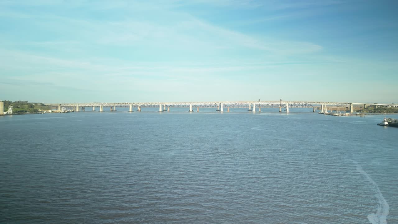 A dynamic aerial zoom captures the Benicia-Martinez Bridge, showcasing its intricate steel framework and the vibrant waterways of Martinez, California, against a backdrop of sky and shoreline.