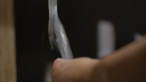 washing kitchen utensils with bubbly sponge and rinsing with tap water - close up