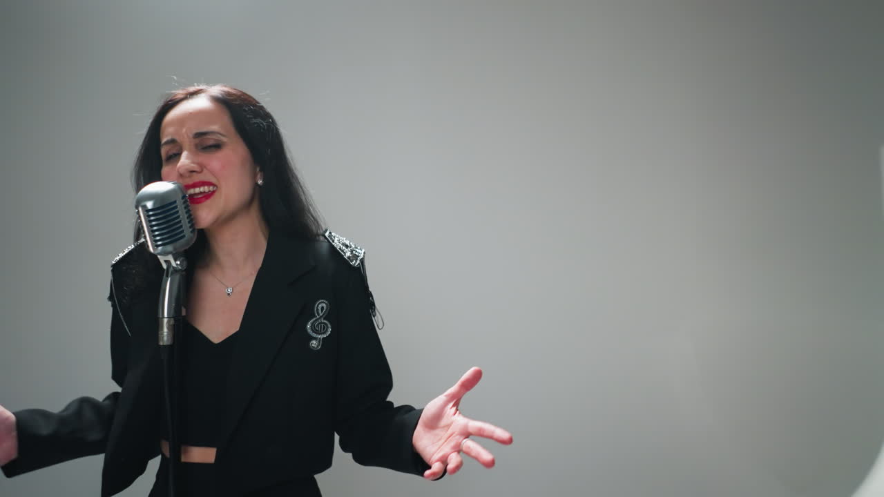 vocalista femenina emotiva en traje negro cantando apasionadamente con gestos de la mano, la cámara dinámicamente acercándose y alejándose sobre un fondo blanco