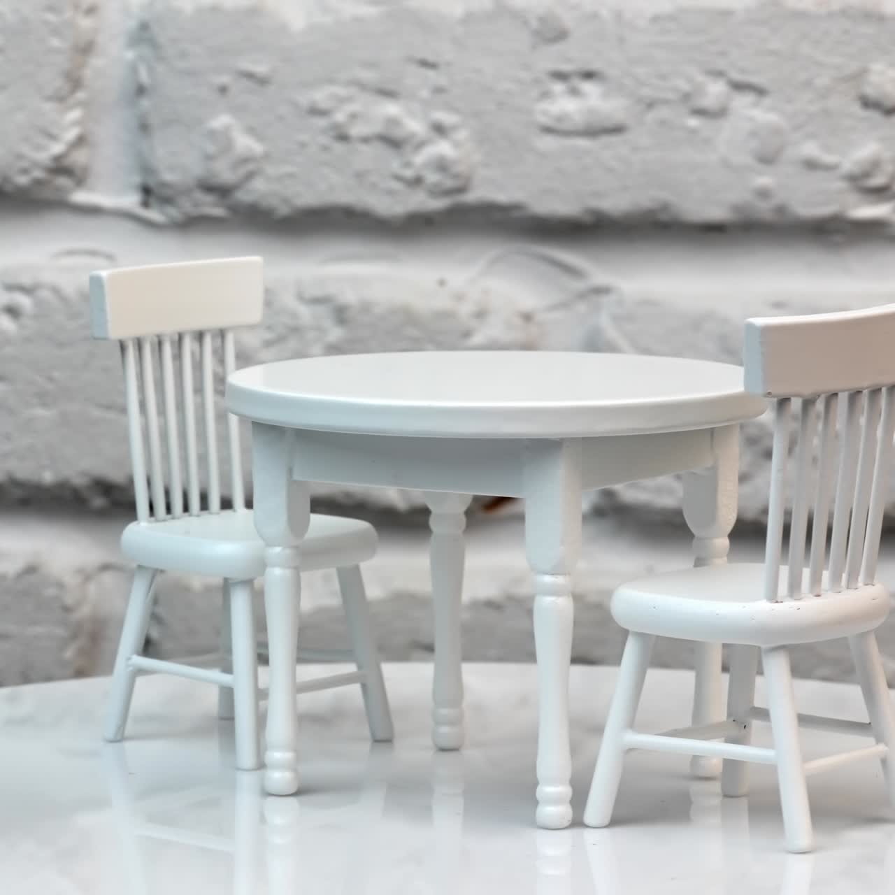 Two wooden chairs and round table between them. Carved toy furniture painted white spinning at the table. Close up