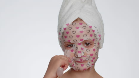 Beautiful-young-smiling-child-girl-applying-cosmetic-moisturizing-face-mask,-use-massage-roller