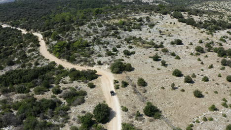 dune buggy travelling along narrow path in vast mountainous landscape, aerial view