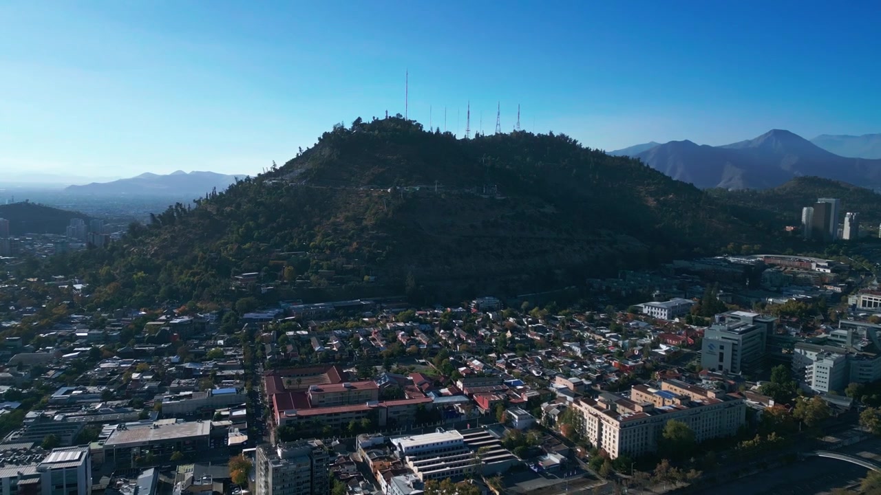 Carrellata che si avvicina al Cerro San Cristóbal, coperto da una fitta foresta nativa, con antenne sulla cima sopra un quartiere residenziale a bassa densità. Santiago, Cile.