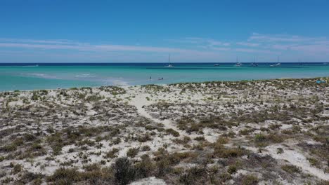 drone aerial view of intact tropical coastline anchored boats and people walking in shallow turquoise water