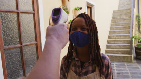 female african american potter wearing face mask and apron getting her temperature measure before en