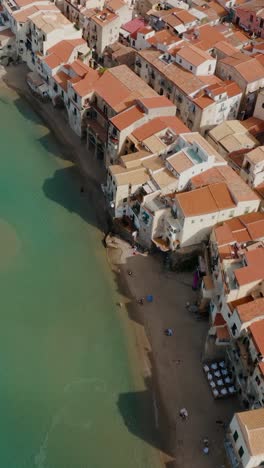 vertical top down aerial drone shot of cefalu beach. flying along the coastline of small historic town in sicily. charming italian heritage.