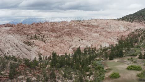 slow rise with drone over rocky crest to reveal open landscape and snowy mountains in the distance