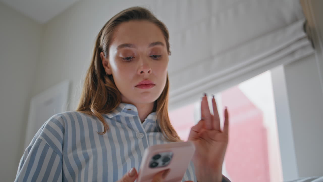 Dissatisfied girl reading cellphone message in light apartment room closeup