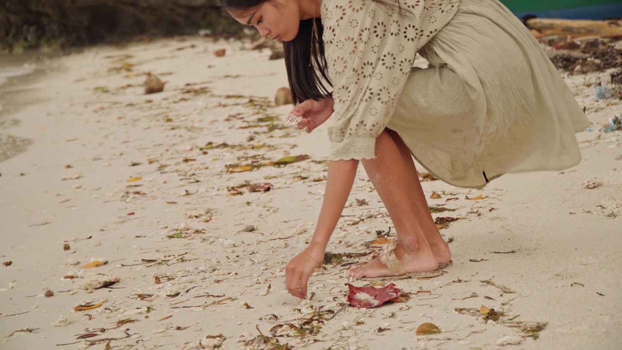 Kaki di pantai berpasir memungut bintang laut, wanita membungkuk untuk mengumpulkan bintang laut kecil di antara rumput laut dan kerang, close-up kaki dan tangan, cahaya lembut yang hangat, suasana hati yang tenang dan kontemplatif, tekstur pasir yang detail.